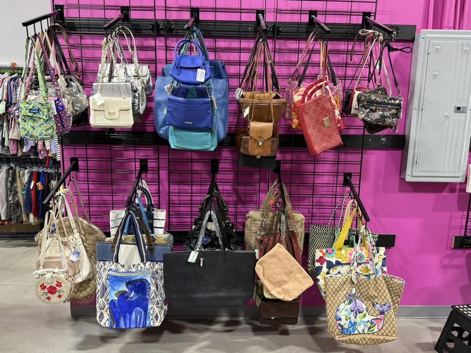 Purses, crossbody bags and totes hanging on a pink display wall at Thrift It Out