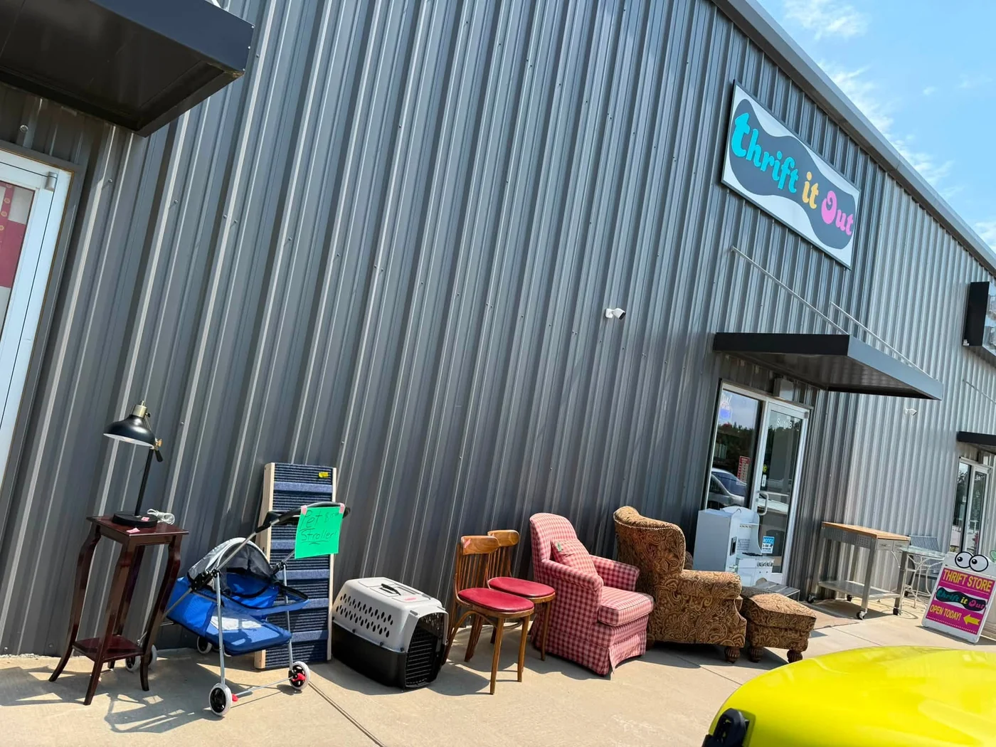 Thrift It Out storefront sign on the metal building exterior, with furniture and other finds displayed outside the door
