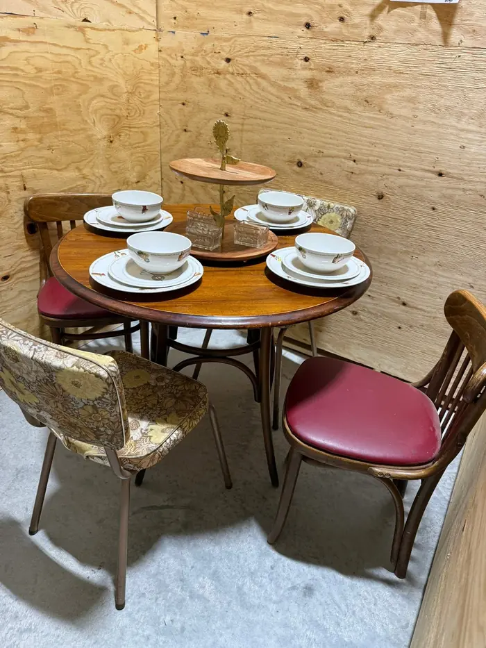 Round wood dining table set with mismatched vintage chairs and dishware