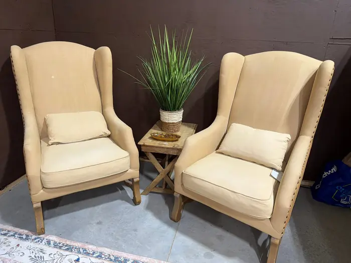 Pair of tan wingback chairs beside a small wood accent table