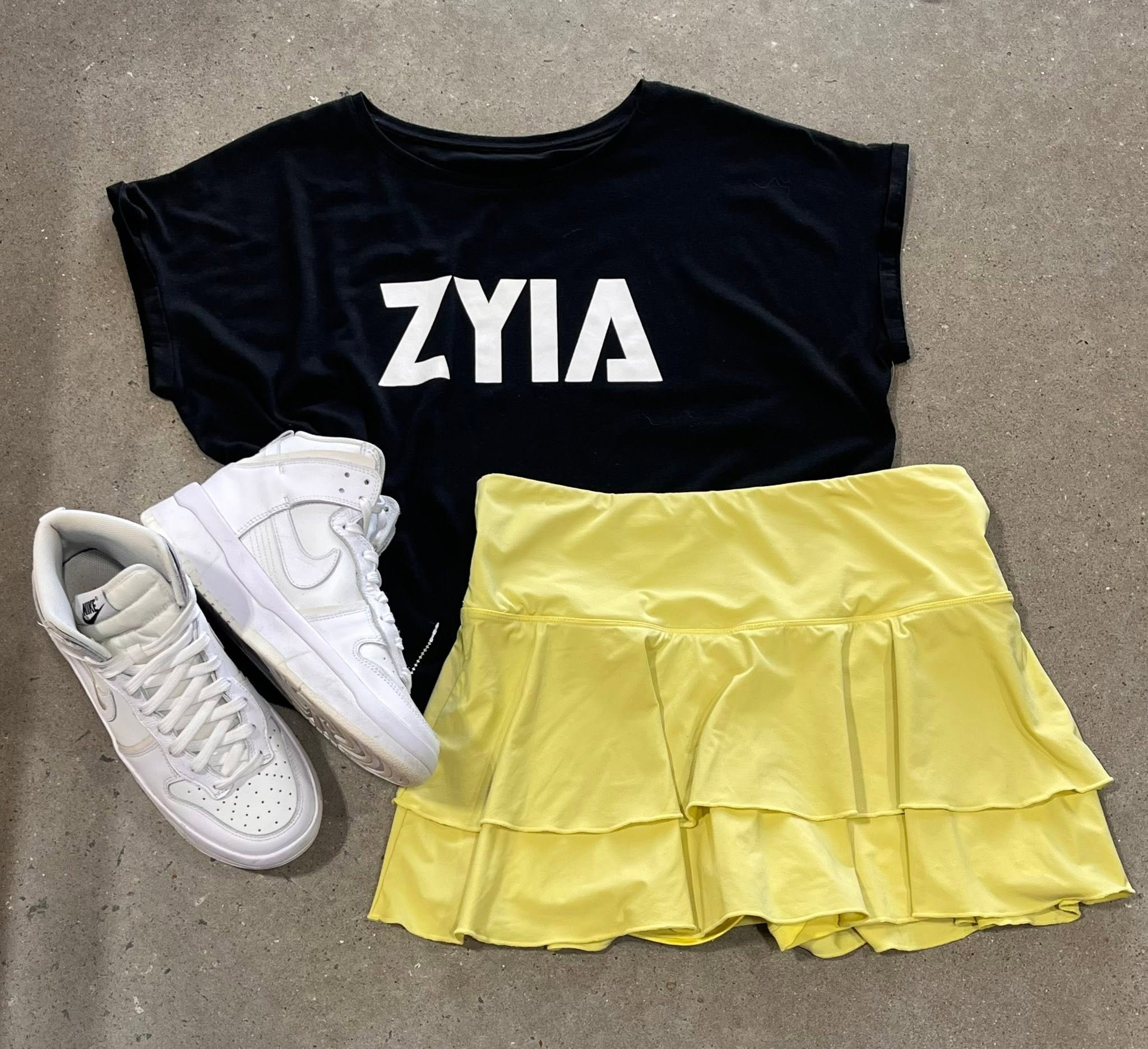 Flat lay of a black graphic T-shirt, yellow ruffle skort and white high-top sneakers