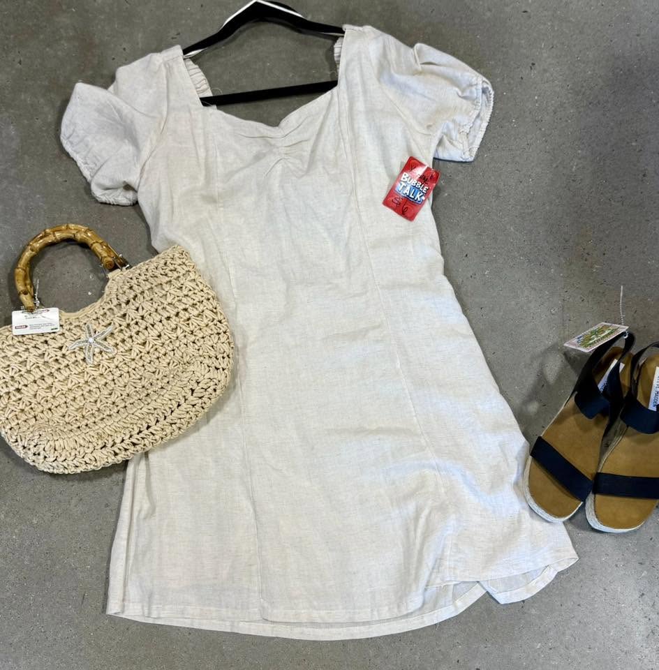 Flat lay of a beige short-sleeve dress with a woven straw handbag and black strap sandals