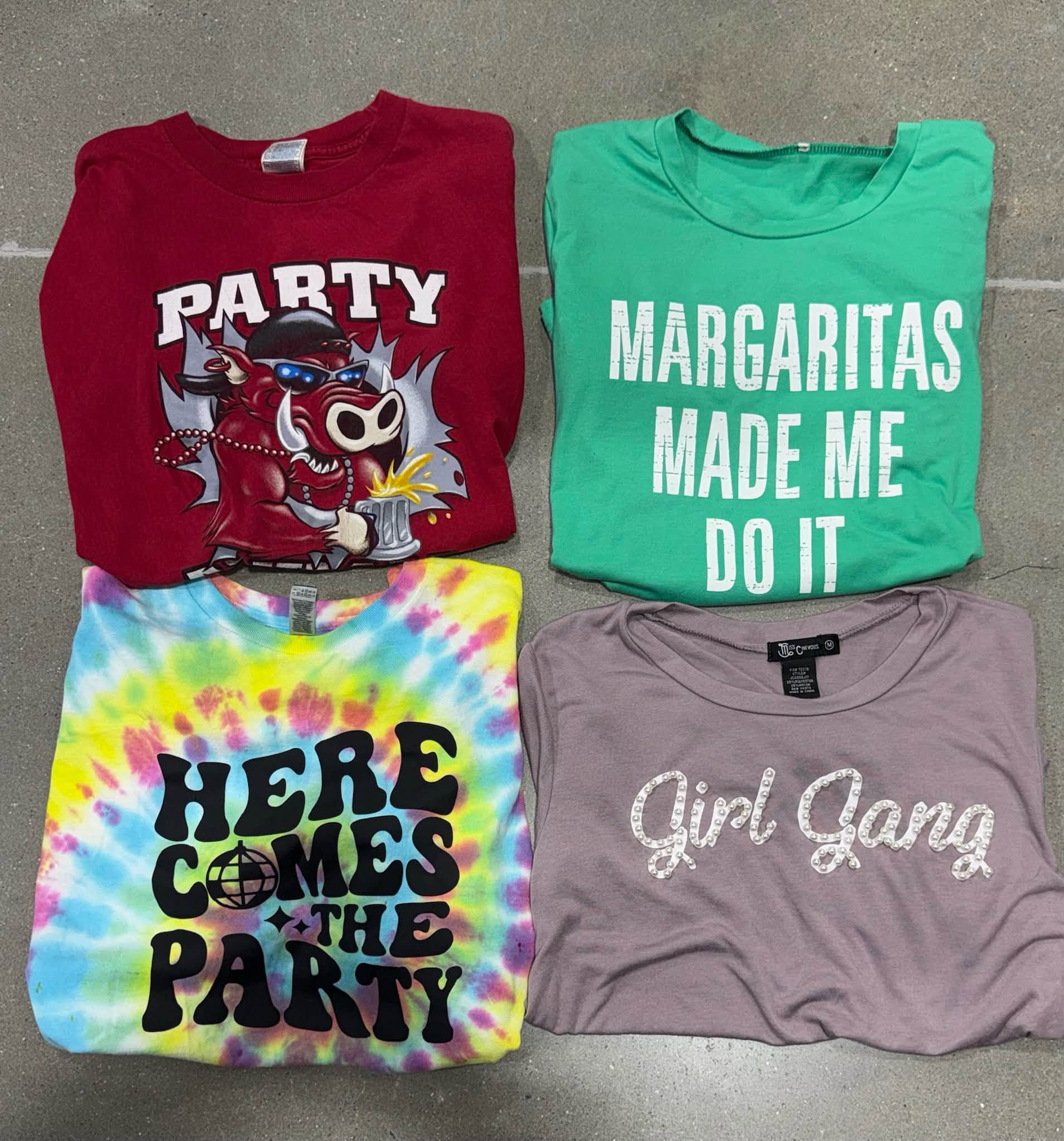 Four folded graphic and tie-dye T-shirts laid out on the floor
