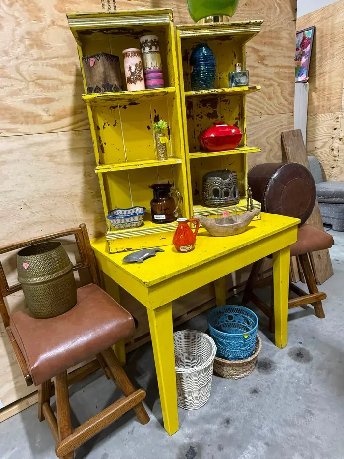 Distressed yellow display shelf and table holding vases and pottery
