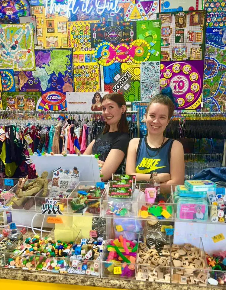 Two staff members smiling behind the checkout counter, surrounded by board games and toys on display